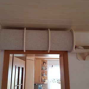 Da der kleine Tunnel so ein begehrter Schlafplatz wurde und sich alle drei da rein gedrängelt haben, musste eine noch eine größere Version her. Der große Tunnel hängt über der Küchentür. Nachteil ist, man braucht immer ein Stuhl um nachzusehen ob einer drin liegt. Ich habe schon überlegt ein Loch in die Mitte reinzubauen.

Der Tunnel ist eigentlich nur eine Röhre aus zwei auf Maß geschnittenen Teppichstücken, welche mit dem Rücken gegeneinander gerollt sind und zwischen den vier Sperrholzspanten fixiert sind. Die Spannten dienen gleichzeitig über eine weitere Sperrholzplatte als Befestigung an der Wand.